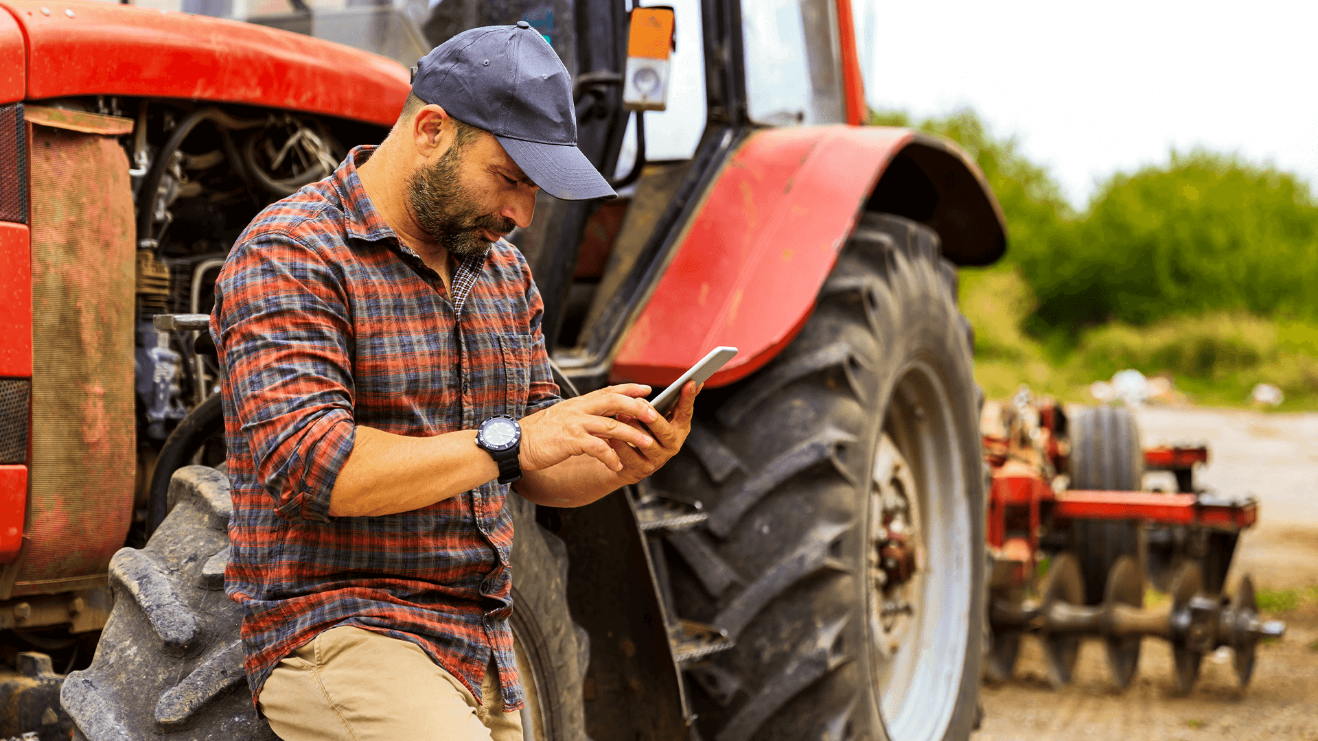 Produtor rural avalia os dados da lavoura para uma gestão financeira eficiente. Ele está apoiado em um trator vermelho. 